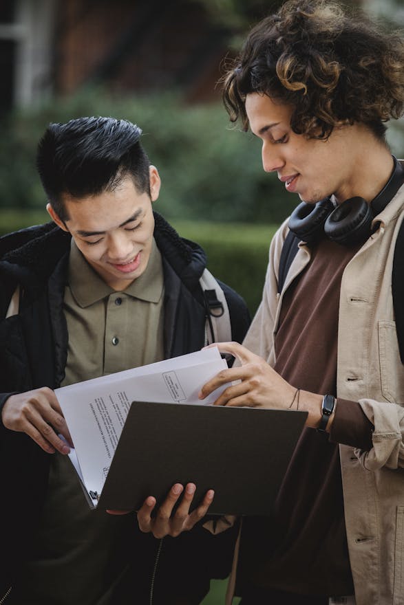 Young multiracial guys in casual clothes standing in street with folder and papers while having conversation in daytime